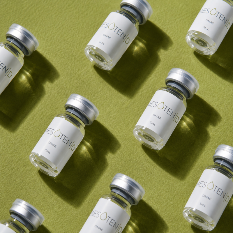 Multiple Mesoten D DMAE 5ml vials arranged on a textured green background